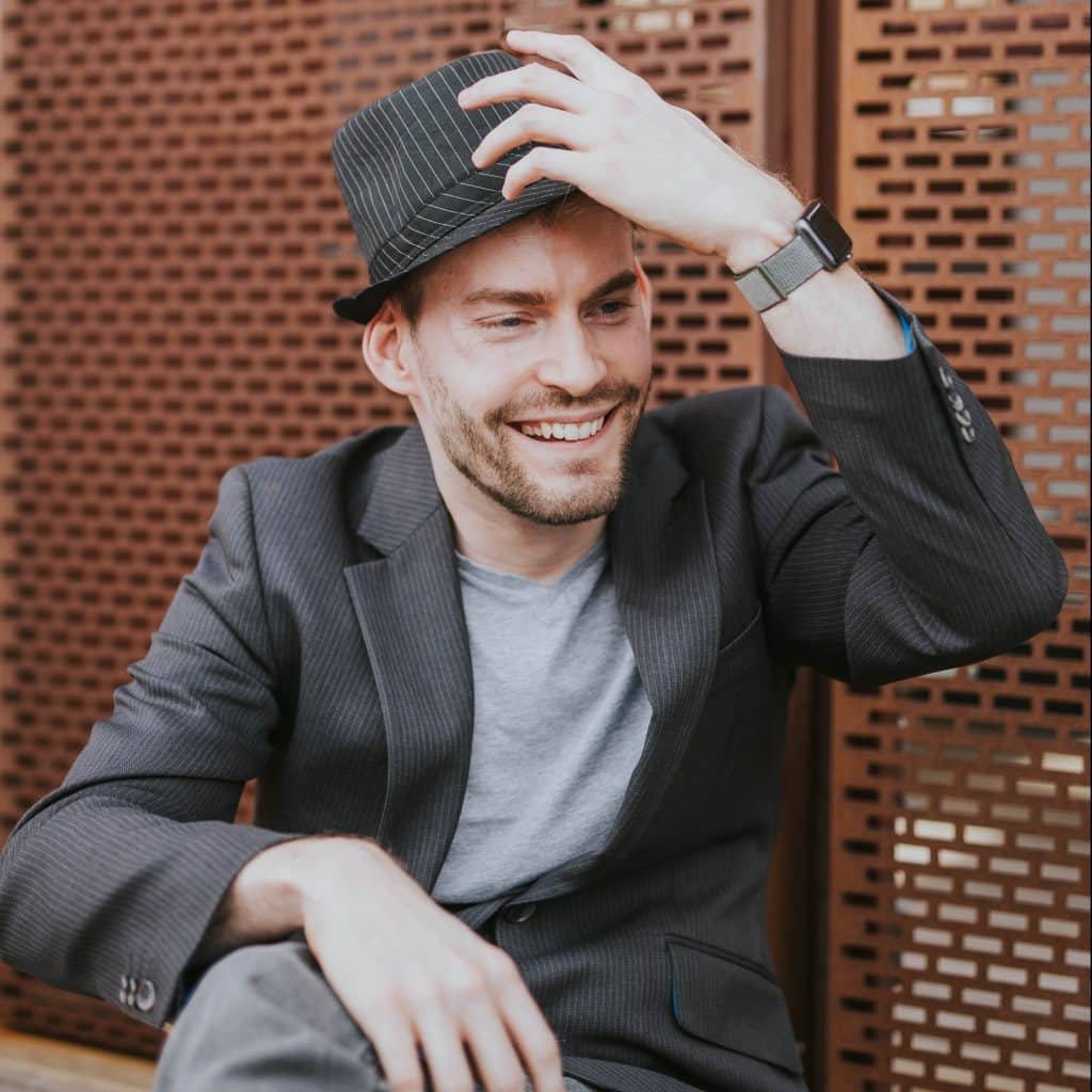 A picture of Dan wearing a suit jacket and trilby hat smiling